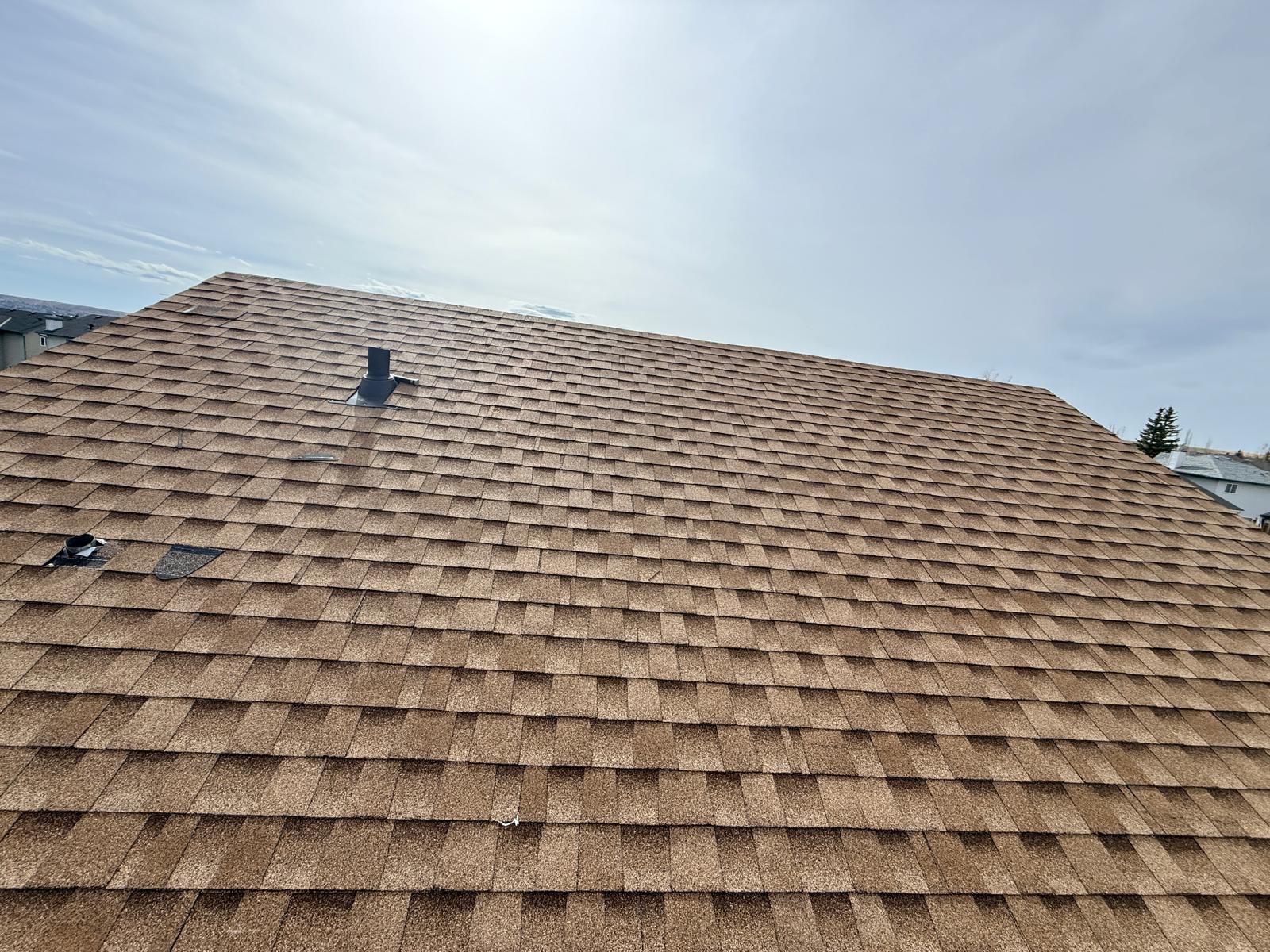 Brown architectural shingles on a long slope with a vent stack, viewed from the eave