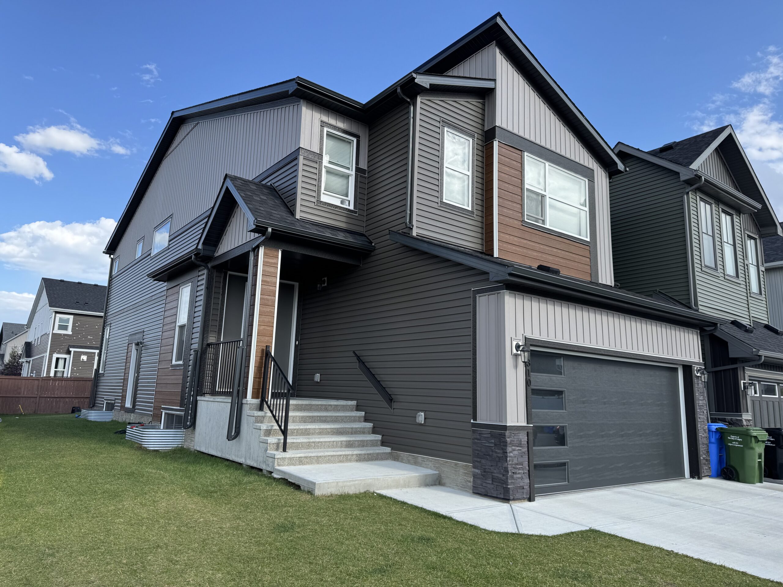 Townhome row in grey vinyl siding with wood-tone accent panels set between the gables