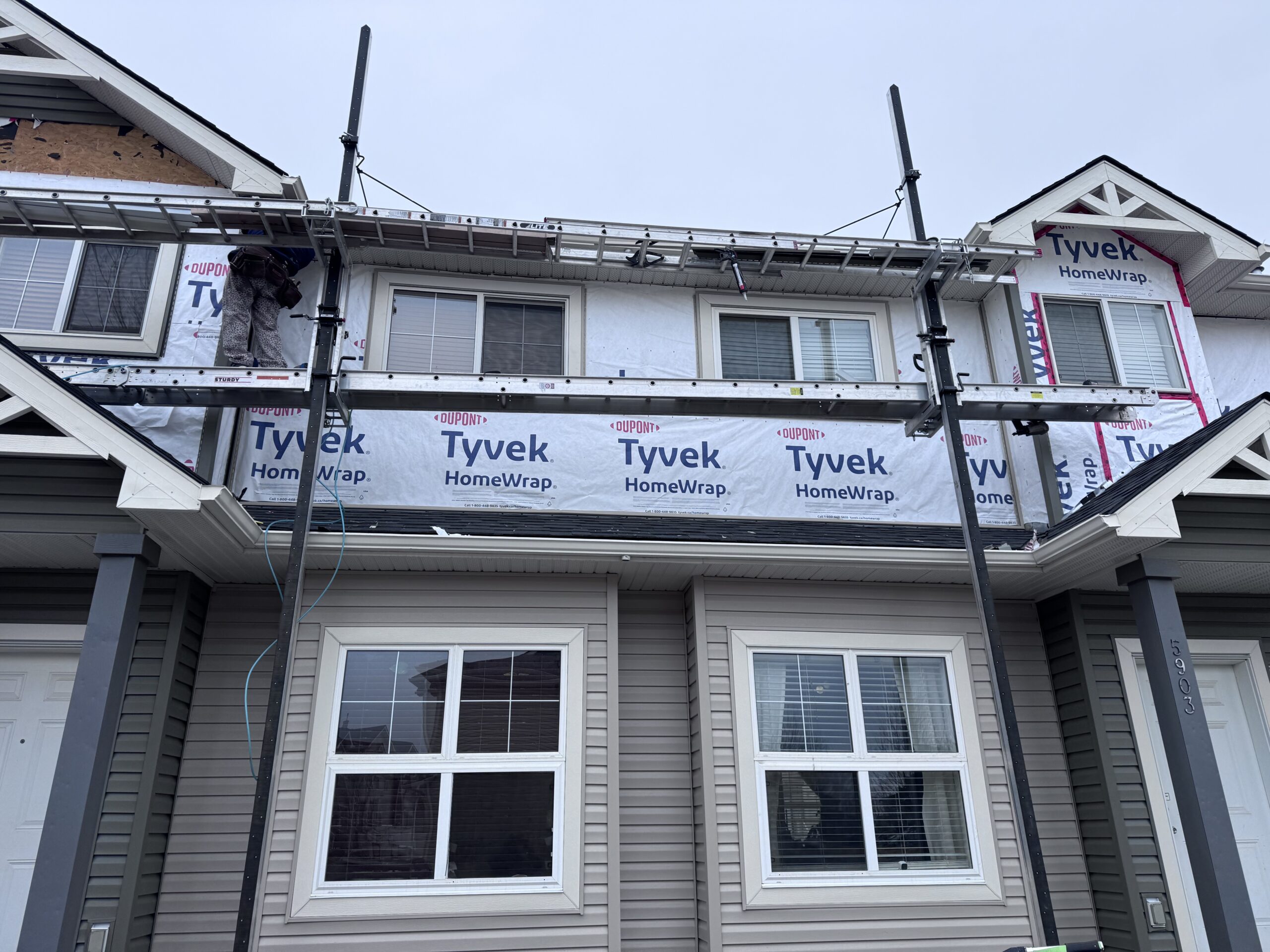 House wrapped in building wrap with scaffolding up, ready for vinyl siding to be installed