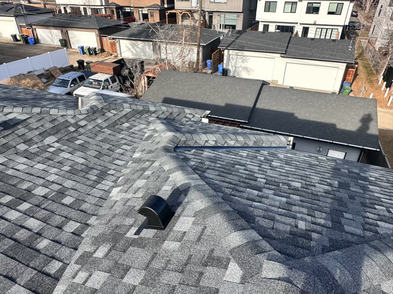 Grey architectural asphalt shingles on a hip roof with a new roof vent and the back lane behind