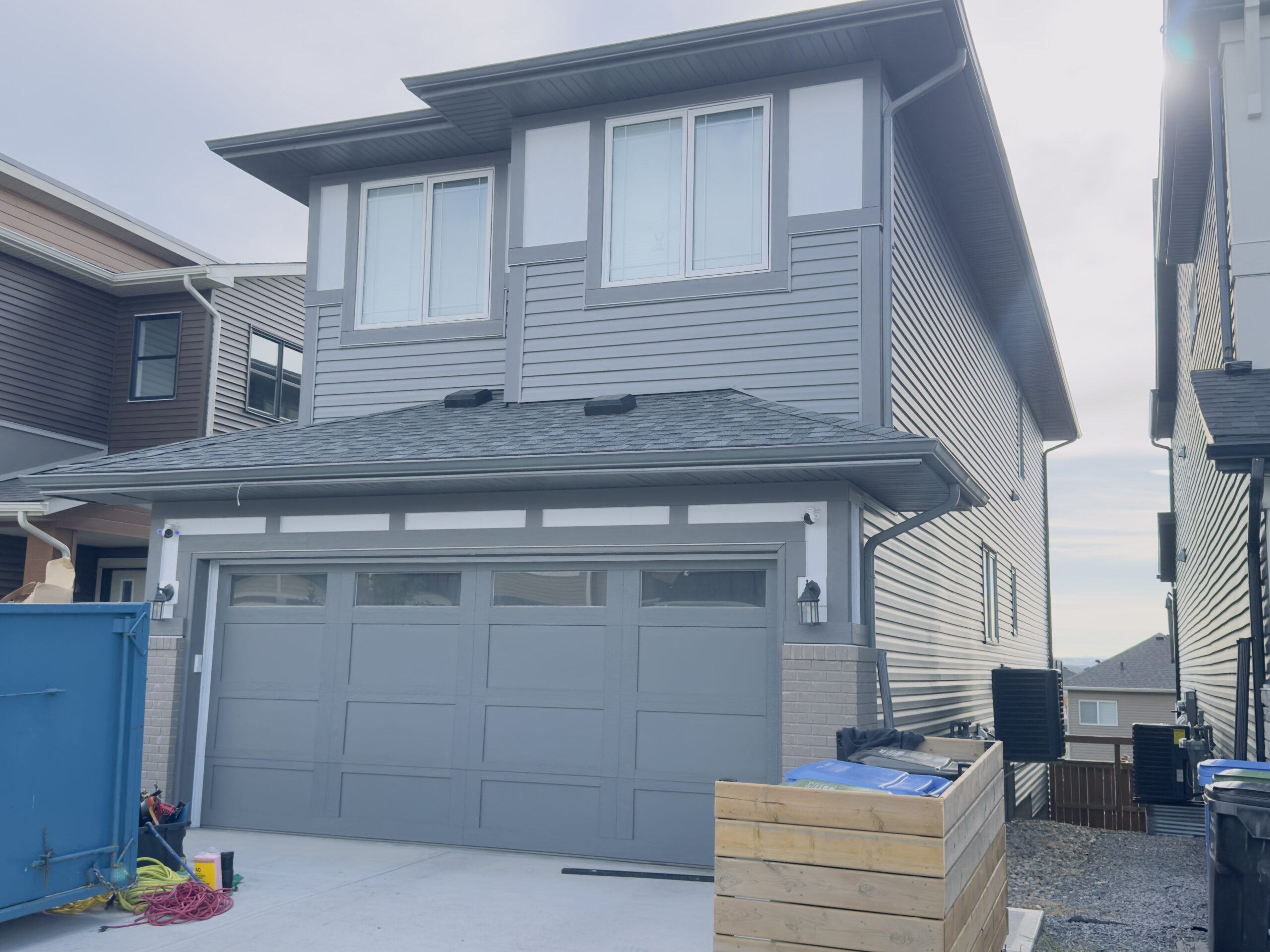 Grey vinyl siding on a two-storey home lit by low sun, with the garage below and trimmed windows above