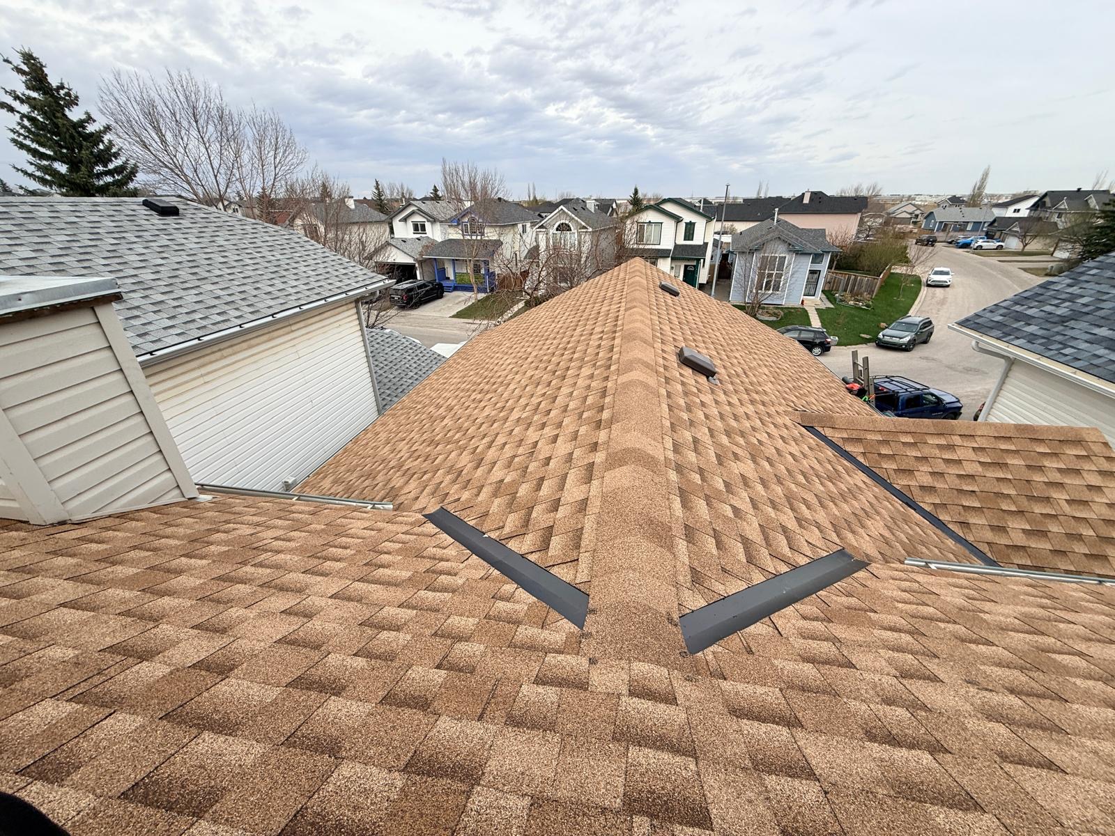 Brown architectural shingles on a hip roof with ridge vents, overlooking a residential street