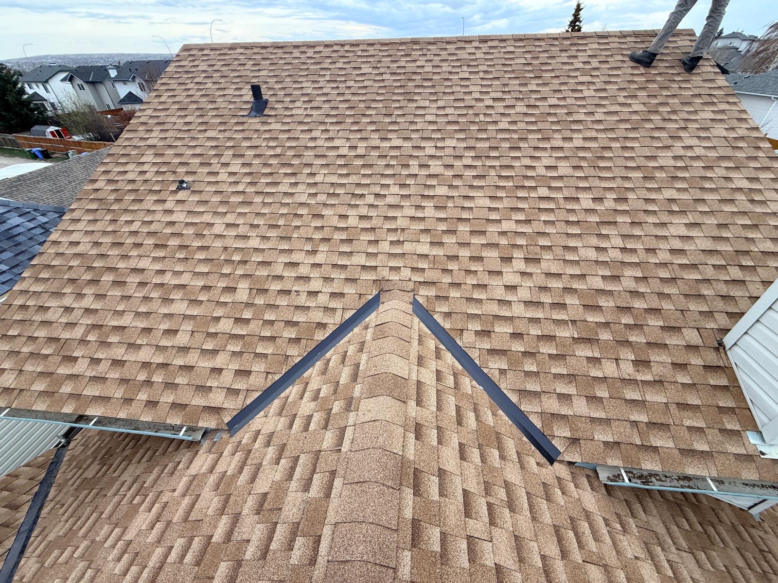 Brown shingles on a hip roof with metal valley flashing and eavestrough at the edge
