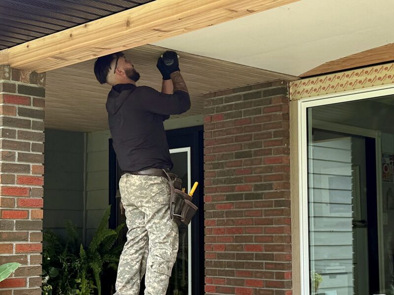 Installer fitting soffit under a covered porch ceiling