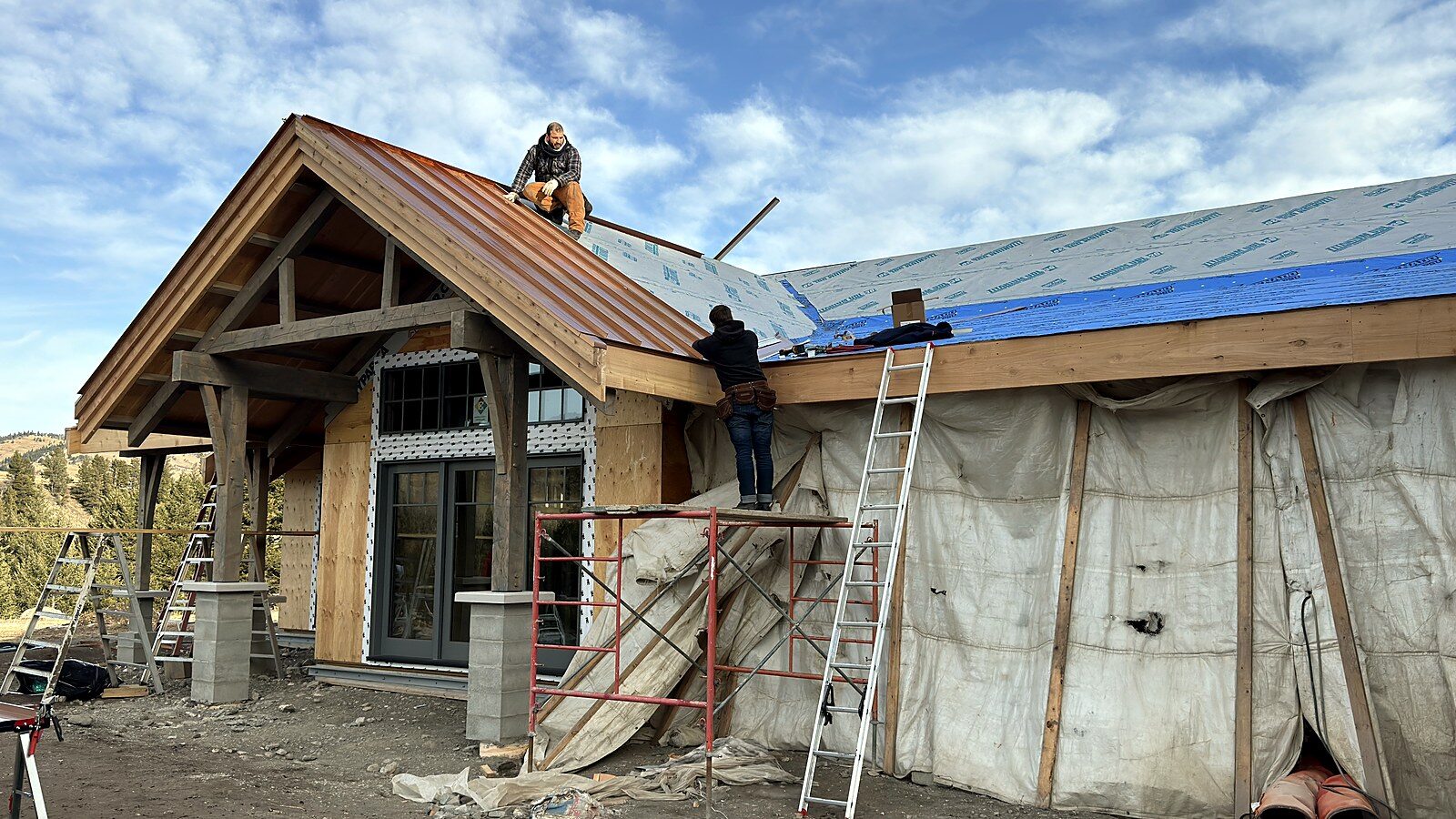 Metal roofing going on over the underlayment of a timber-frame house, with the deck fully visible