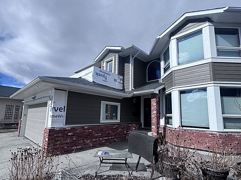 Two-storey home with bay windows part-way through a re-side, weather barrier still exposed
