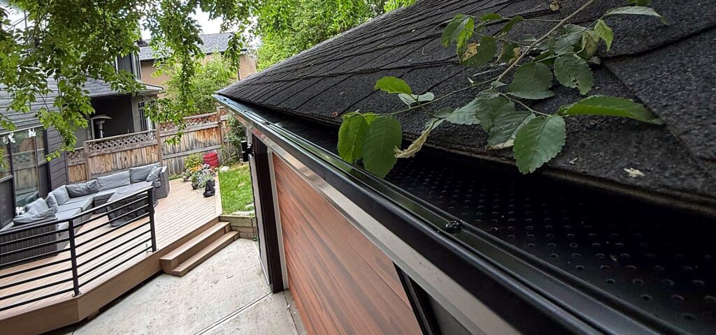 Perforated aluminum gutter guard fitted on an eavestrough beneath overhanging trees on a Calgary garage roof
