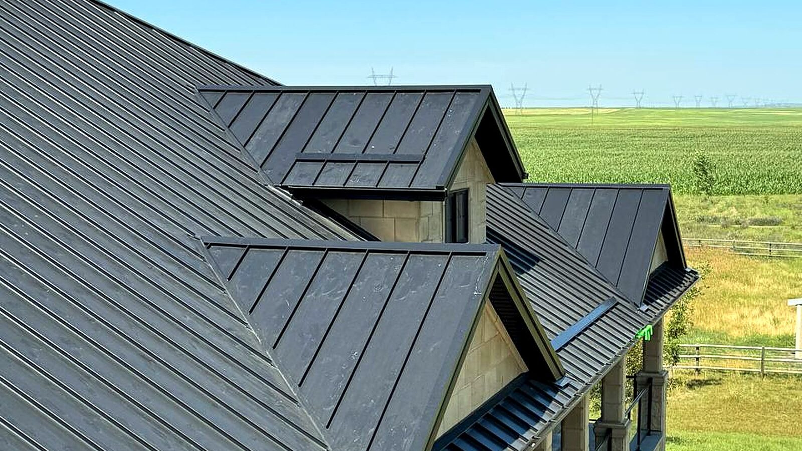 Dark standing seam metal roof on a farmhouse with prairie fields behind