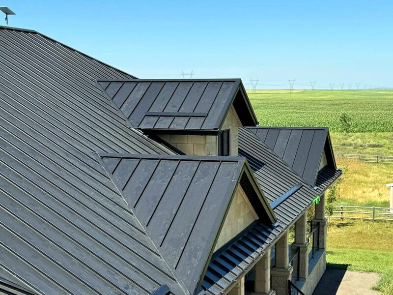 Dark standing seam metal roof on a farmhouse with prairie fields behind
