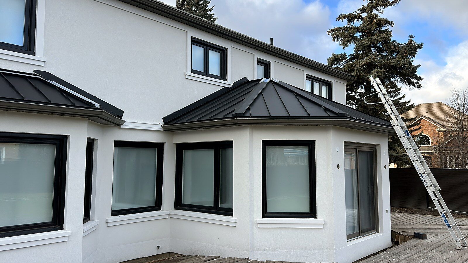 Two-storey stucco house with black standing seam metal roof accents over the bay windows, winter