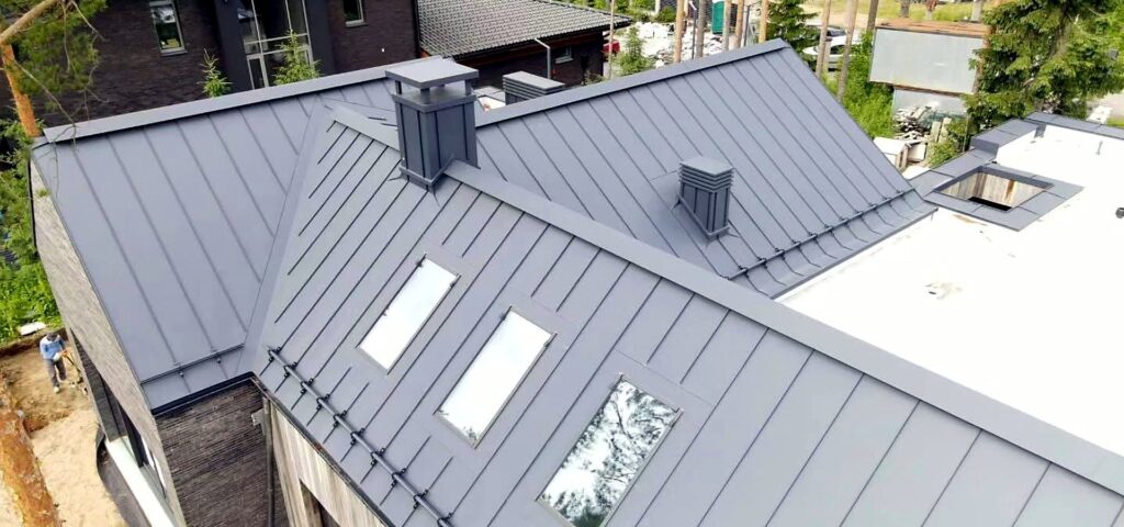 Drone view of a dark grey standing seam metal roof with skylights and chimneys