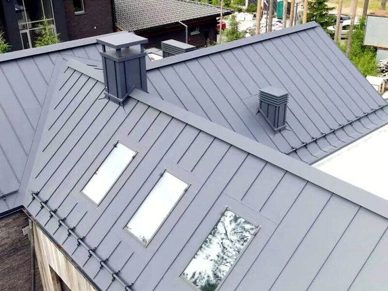 Drone view of a dark grey standing seam metal roof with skylights and chimneys