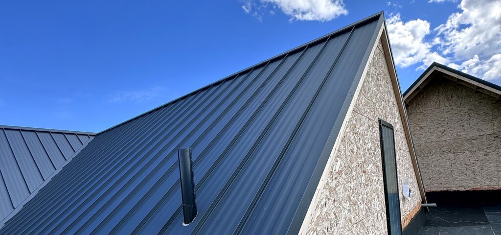Close view of standing seam metal roof panels and a vent stack against a blue sky