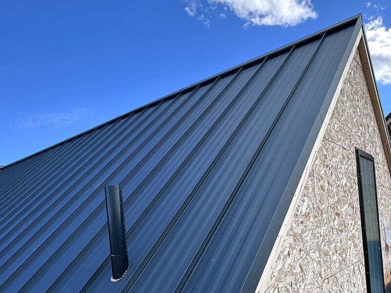Close view of standing seam metal roof panels and a vent stack against a blue sky